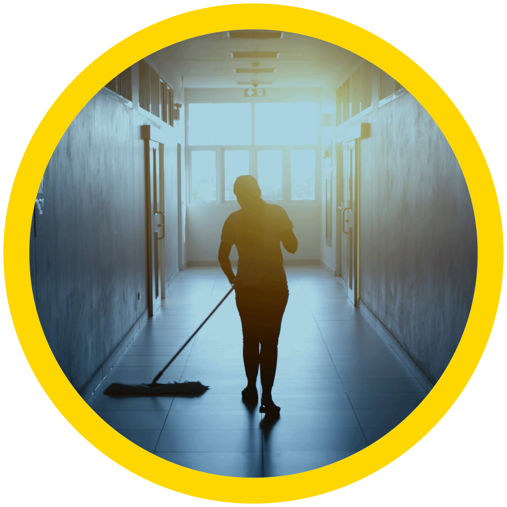 A janitor is walking down an office hallway mopping the tile floors.
