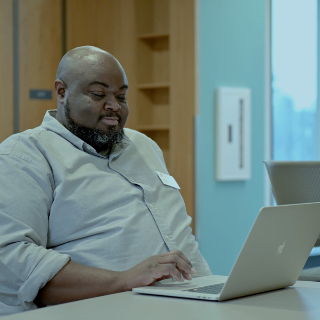 A male is sitting at a desk in a conference room scrolling on his Macbook Pro laptop.